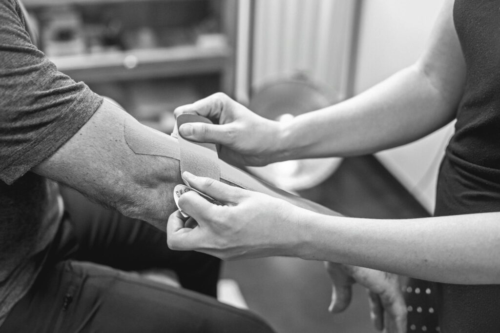 Close-up of kinesiology tape being applied on an elbow for therapeutic support in a healthcare setting.